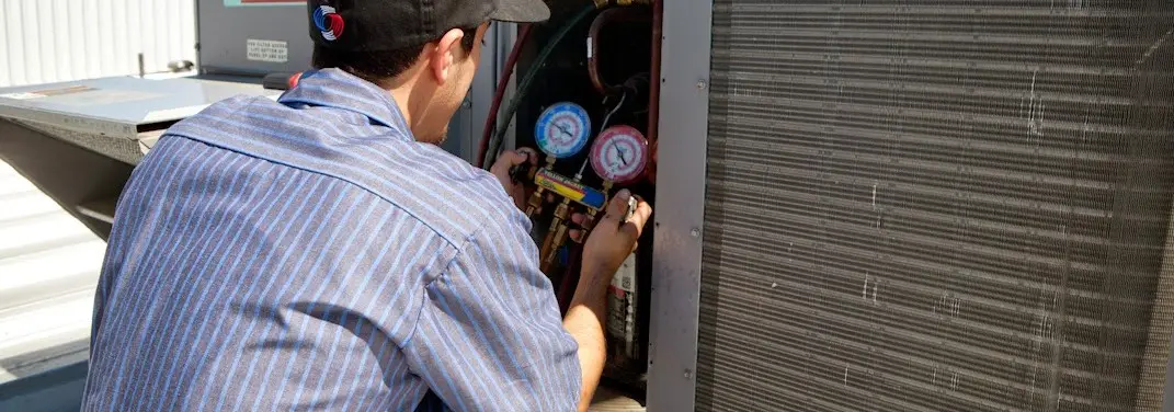 HVAC technician servicing a condenser unit in Bryan